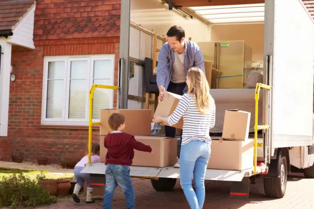 A family of four unpacking a moving truck full of boxes at their new home.