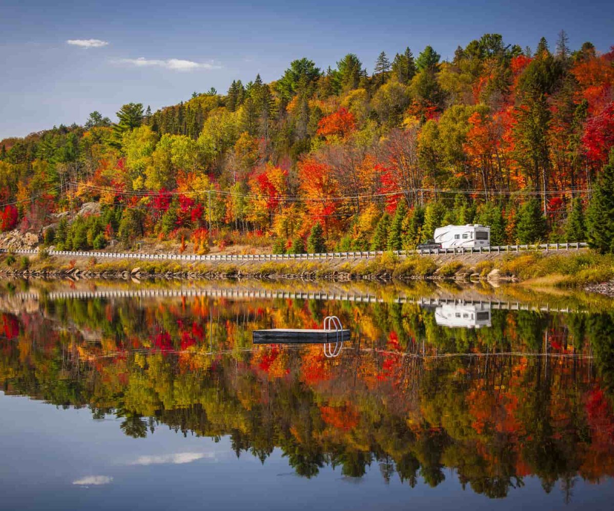 An RV driving past a lake in the fall.