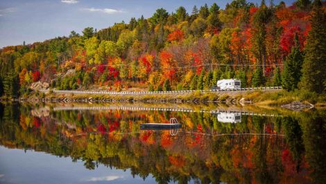 An RV driving past a lake in the fall.