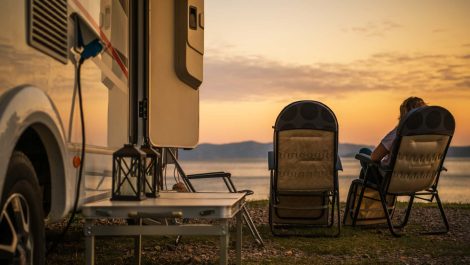 An RV parked lakeside at sunset with a retired couple enjoying the view.