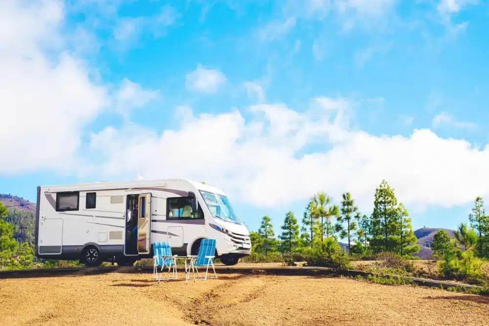 An RV with two chairs next to the side of the road on an overlook