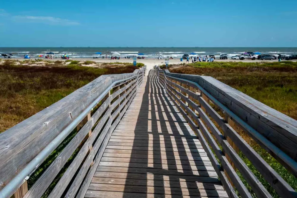 Boardwalk leading to the beach, which has many tents, cars, and visitors.