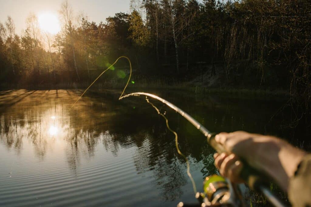 An angler throws bait from his fishing rod into the water as the sun sets