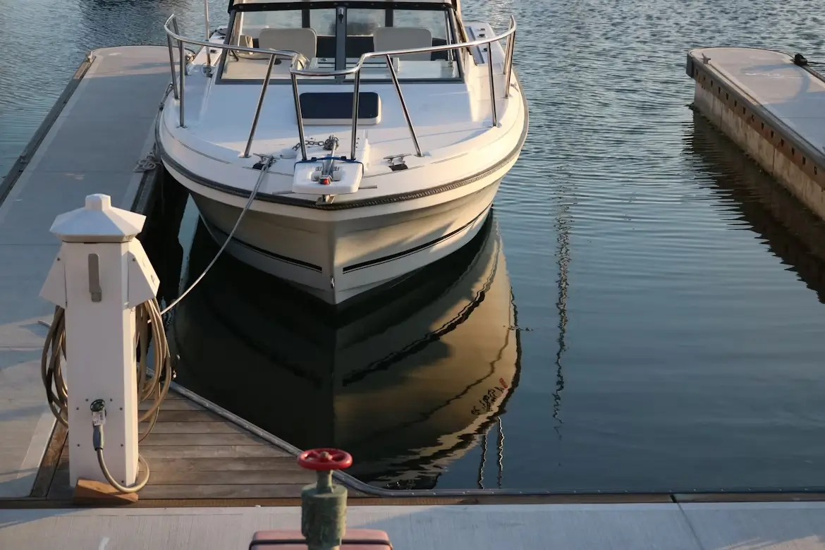 Front view of a white motorboat docked at a marina with calm water reflecting the boat’s hull.