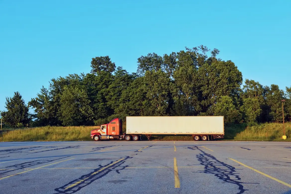 A red semi-truck with a white trailer parked in an empty lot near.