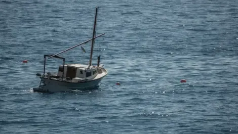 A small fishing boat anchored alone in calm, open blue water with a few floating buoys nearby.