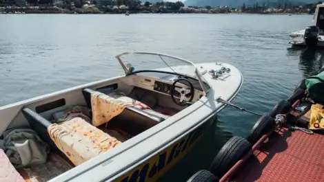 A small motorboat docked at a pier, with floral blankets on the seats and calm lake waters.