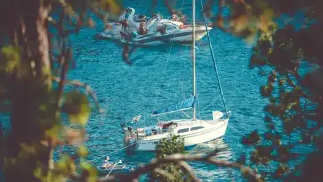 Two boats anchored on a serene blue lake, viewed through tree branches.
