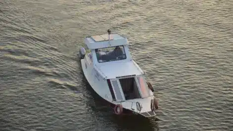 A small white cabin boat cruising through calm water during sunset or early evening.