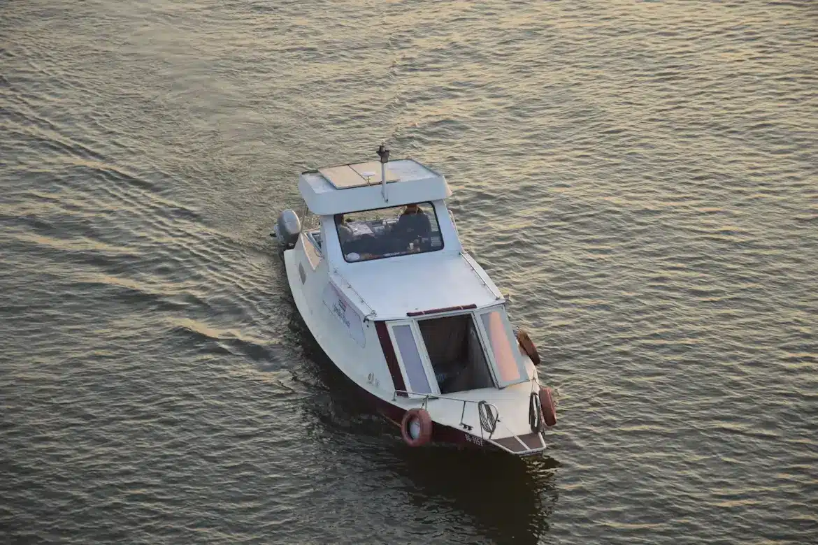 A small white cabin boat cruising through calm water during sunset or early evening.