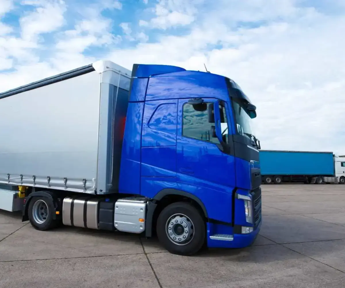 Blue semi-truck parked in a large fleet parking lot under a cloudy sky.