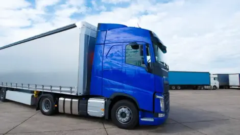 Blue semi-truck parked in a large fleet parking lot under a cloudy sky.
