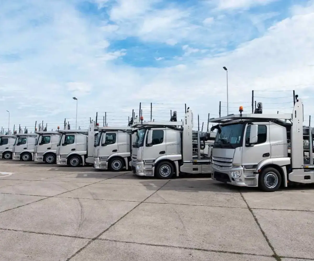Row of silver trucks parked in a large outdoor truck parking lot.