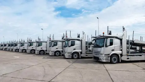 Row of silver trucks parked in a large outdoor truck parking lot.