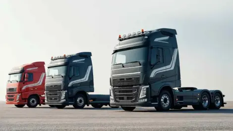 Three semi-trucks parked on a wide open parking lot under a clear sky.