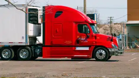 Red semi-truck with white refrigerated trailer parked in a lot.