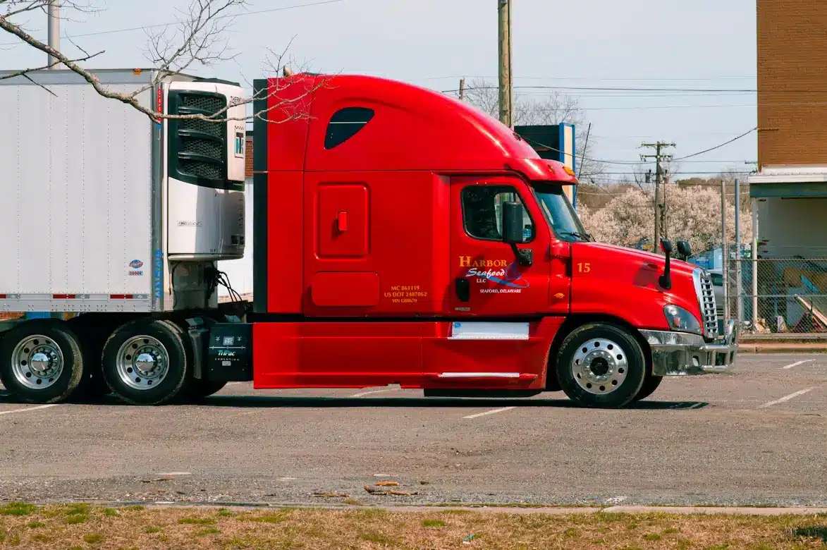 Red semi-truck with white refrigerated trailer parked in a lot.