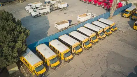 Aerial view of parked school buses and trucks in a lot.
