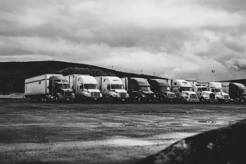 Row of semi-trucks parked in a lot under cloudy skies.