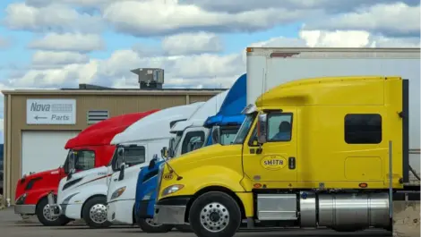 Row of colorful trucks parked side by side in a lot near a parts building.