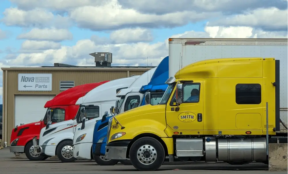 Row of colorful trucks parked side by side in a lot near a parts building.