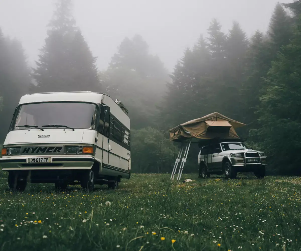 RV and pickup truck with rooftop tent at a foggy forest campsite.