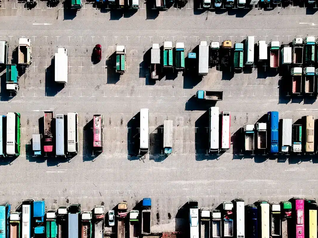 Aerial view of a large truck parking lot with multiple rows of parked semi-trucks, trailers, and a few smaller vehicles.