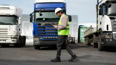 A man inspecting documents in a truck yard.