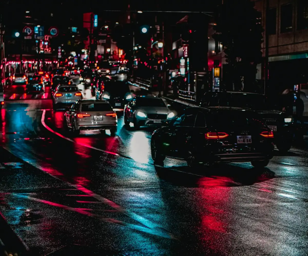 Cars driving on a wet city street at night.