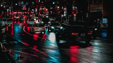 Cars driving on a wet city street at night.