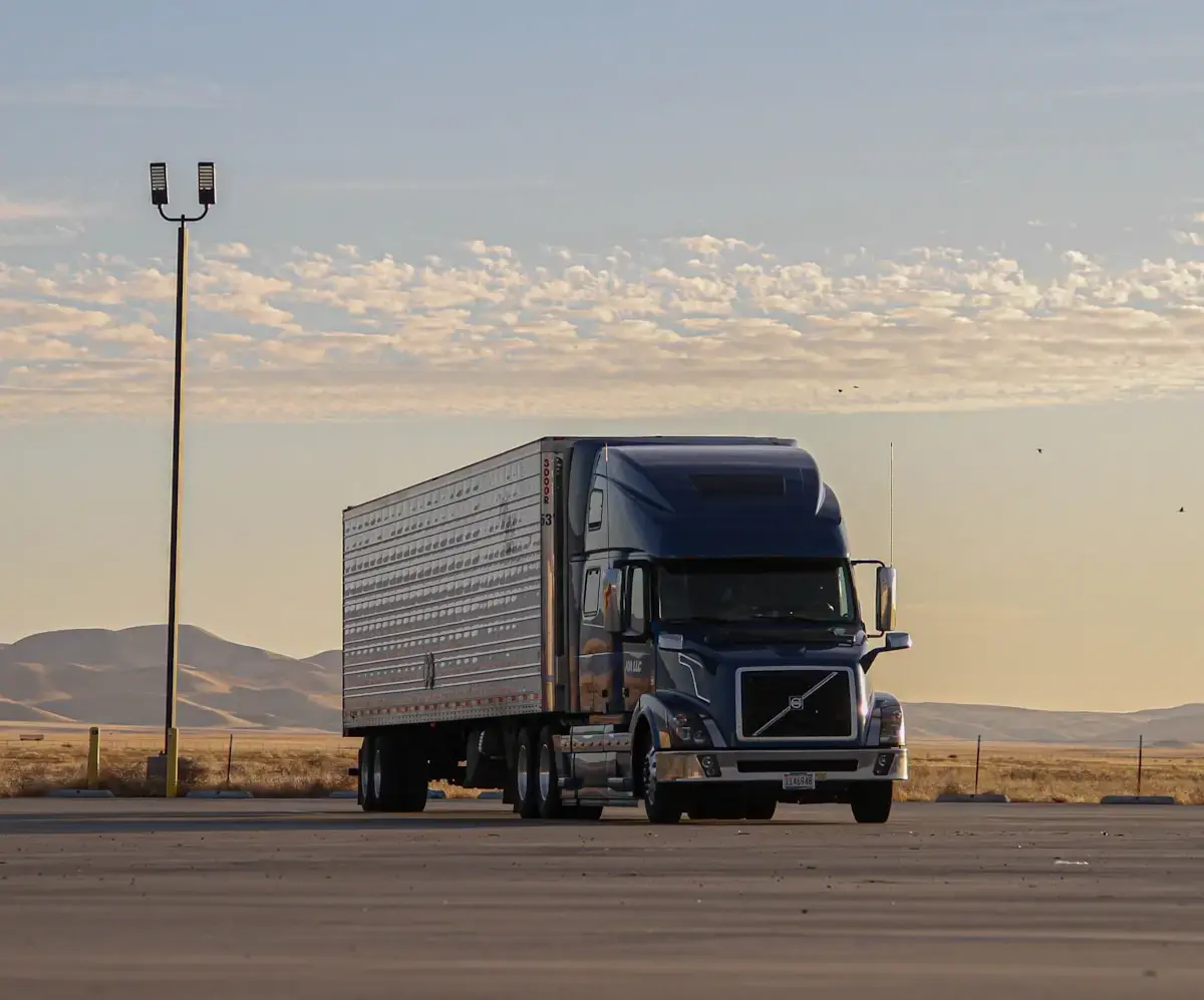 Blue truck parked in an open lot at sunset with mountains in the background.
