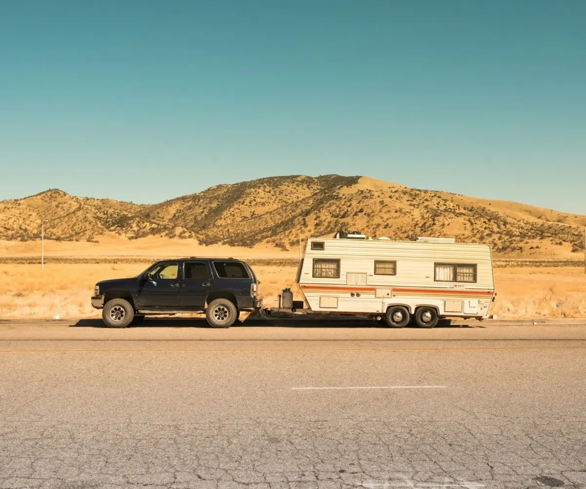 Black SUV towing a beige travel trailer parked safely along a highway.