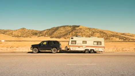 Black SUV towing a beige travel trailer parked safely along a highway.