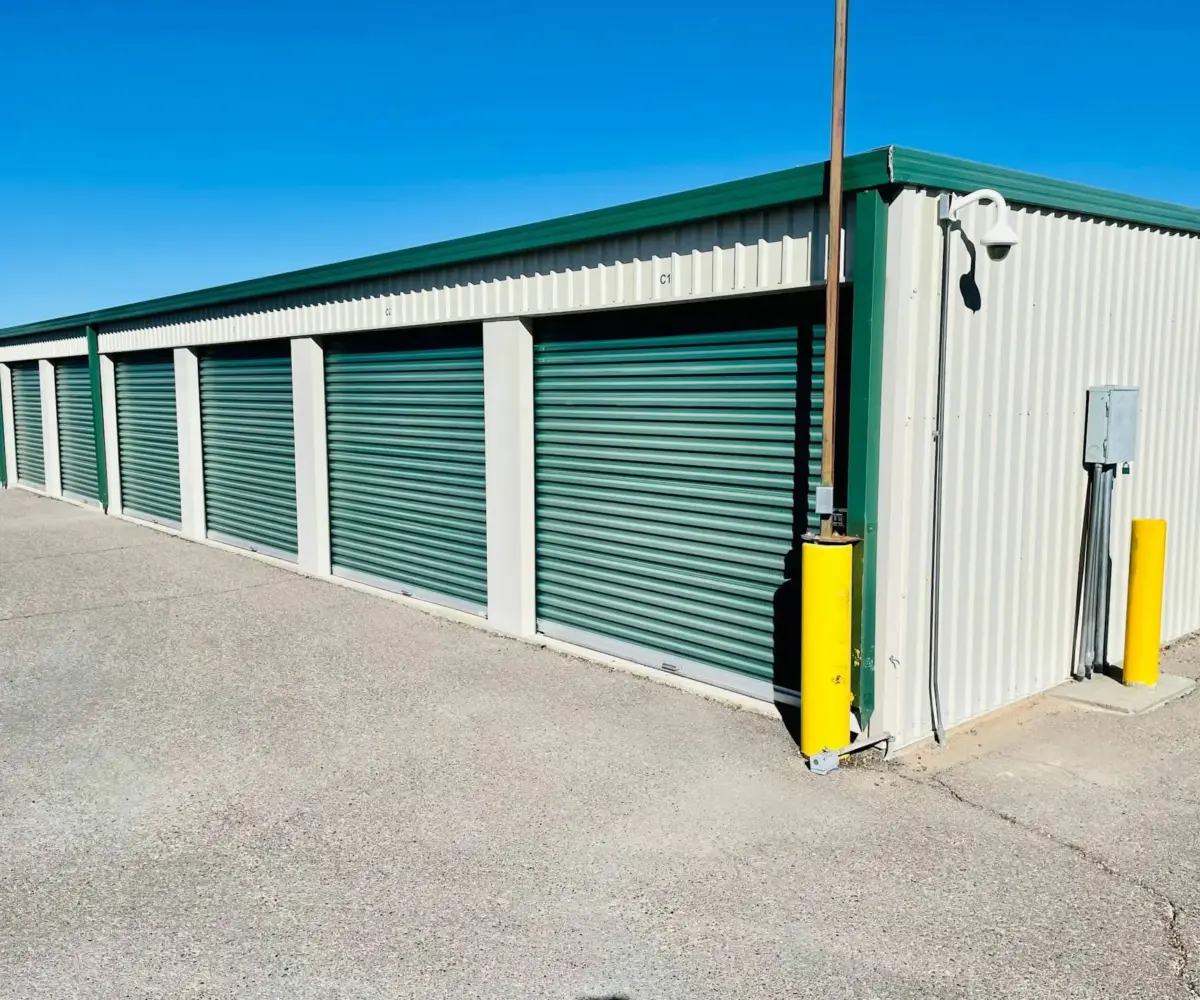 Outdoor self-storage units with green roll-up doors under a clear blue sky.