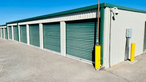 Outdoor self-storage units with green roll-up doors under a clear blue sky.