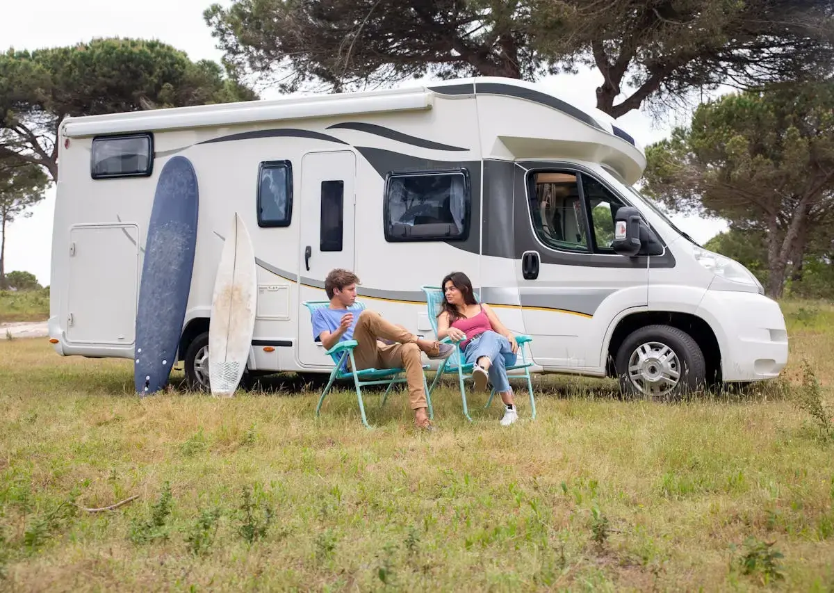 Motorhome parked on grass with surfboards and camping chairs outside.