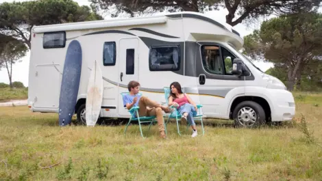 Motorhome parked on grass with surfboards and camping chairs outside.