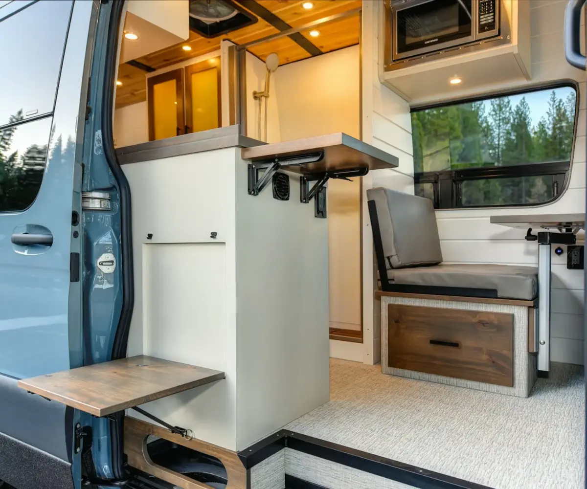 Modern camper van interior with compact kitchen, foldable table, and built-in storage.