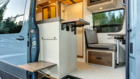 Modern camper van interior with compact kitchen, foldable table, and built-in storage.