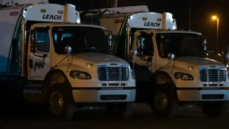 Two white trucks parked side by side at night under streetlights.