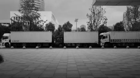 Three commercial trucks parked in a row outside an logistics facility.