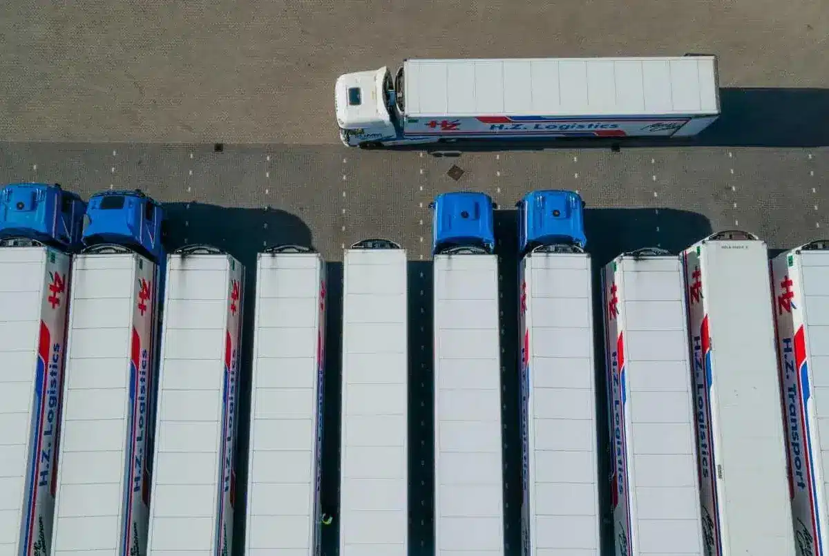 Aerial view of parked logistics trucks in a lot with one truck driving past.