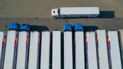 Aerial view of parked logistics trucks in a lot with one truck driving past.