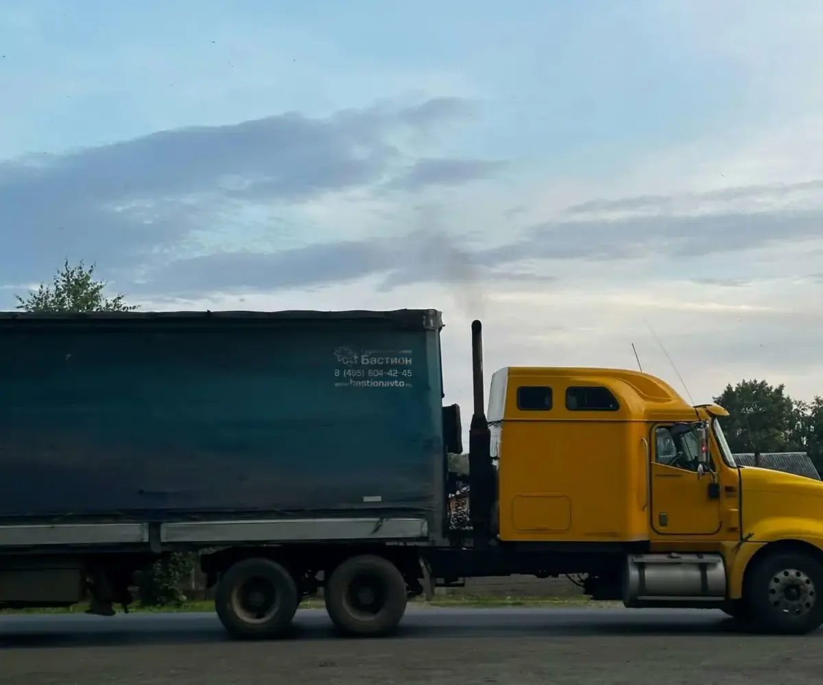 Yellow semi-truck with blue trailer parked outdoors.