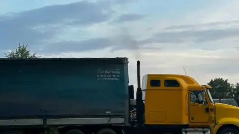 Yellow semi-truck with blue trailer parked outdoors.