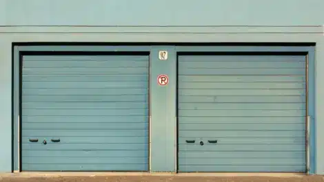 Two closed blue garage-style self storage units with a "no parking" sign in the middle, representing storage facilities as a potential investment option.