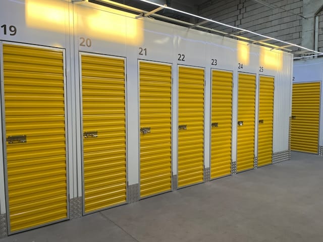 Row of indoor yellow storage unit doors in a well-lit facility.