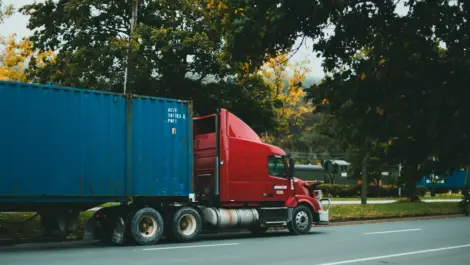 Red semi-truck hauling blue container on roadside.