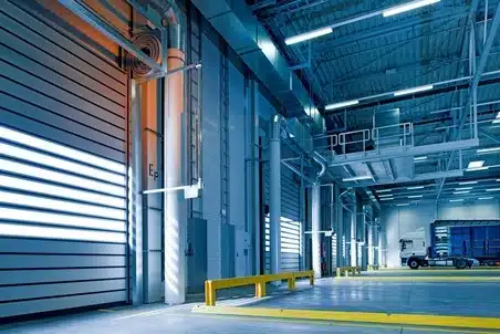 Indoor truck parking area with loading bays, safety barriers, and a parked commercial truck under bright industrial lighting.
