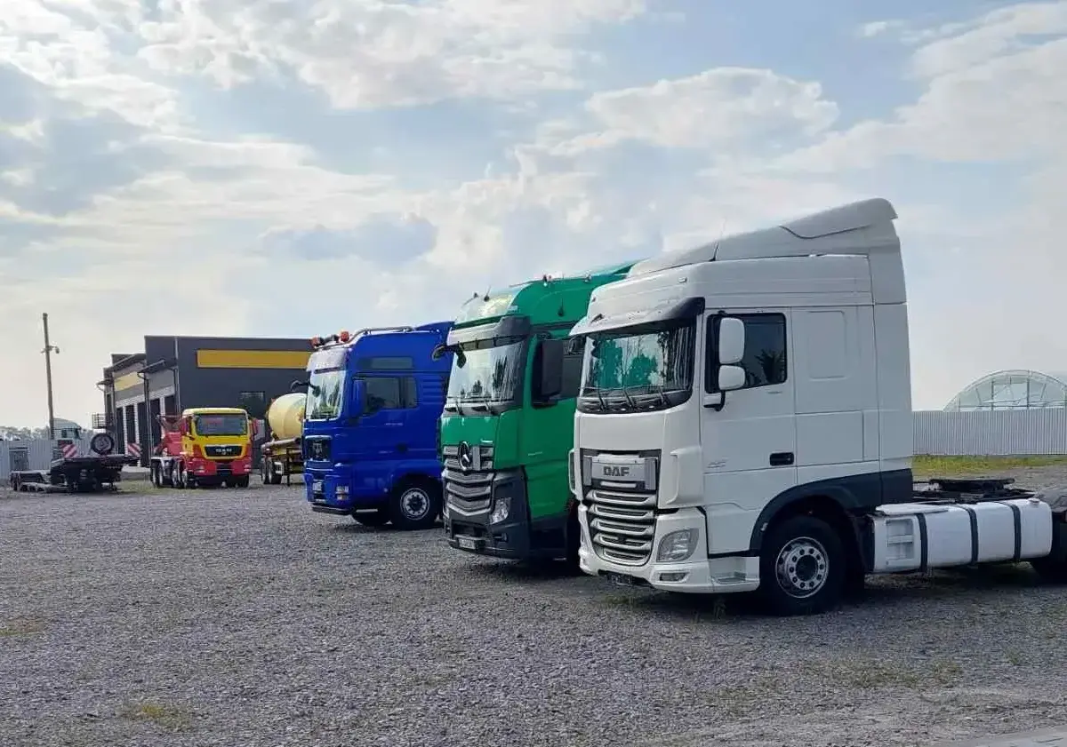 Several trucks parked in a lot near a building under a cloudy sky.